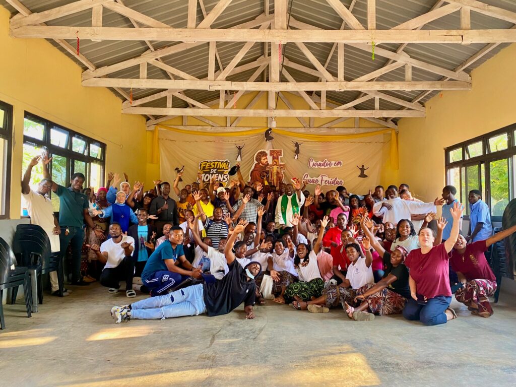 Foto de grupo dos participantes do Festival de Jovens em Dombe, diante do painel “Curados em Suas Feridas”.