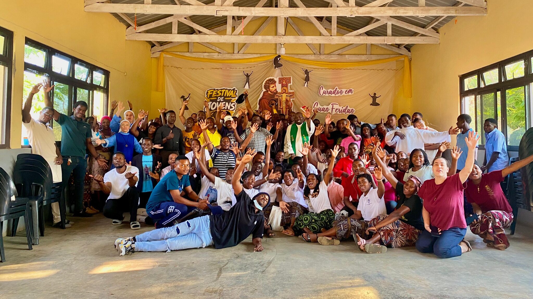 Foto de grupo dos participantes do Festival de Jovens em Dombe, diante do painel “Curados em Suas Feridas”.