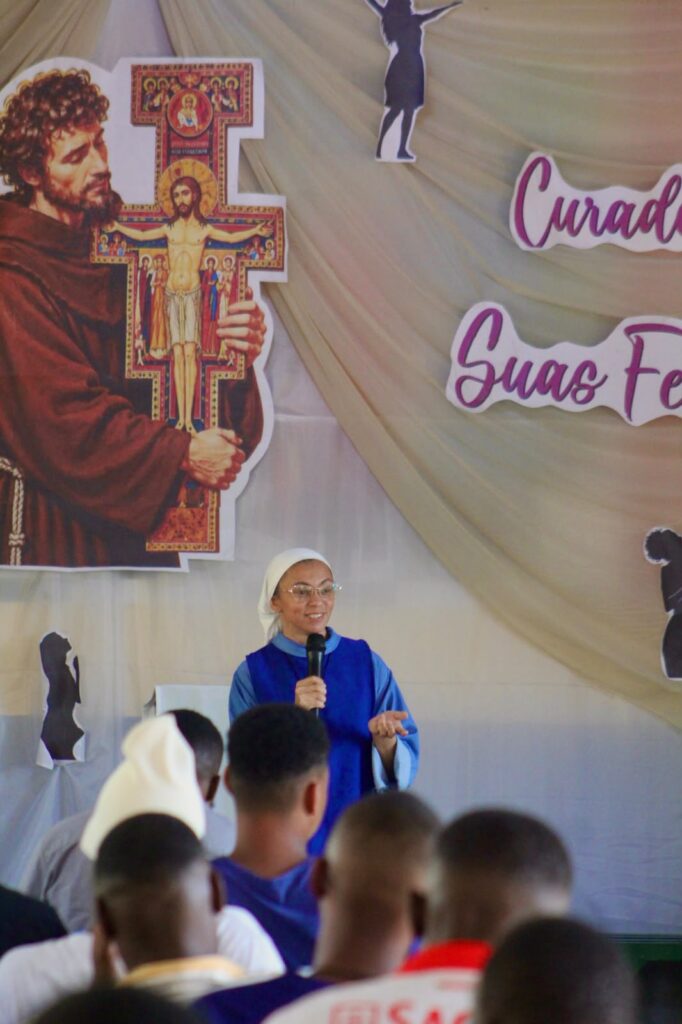 Missionária fala aos jovens diante do painel do festival em Dombe.